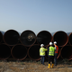 Workers stand in front of stacked pipes for a natural gas pipeline.